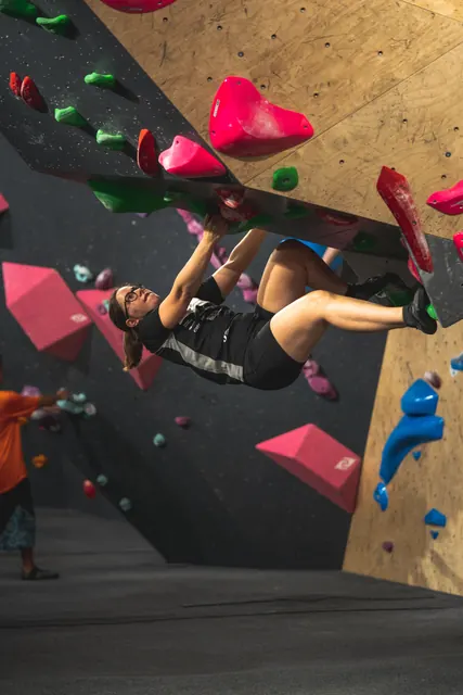 A climber hanging upside down on an overhang with pink holds.