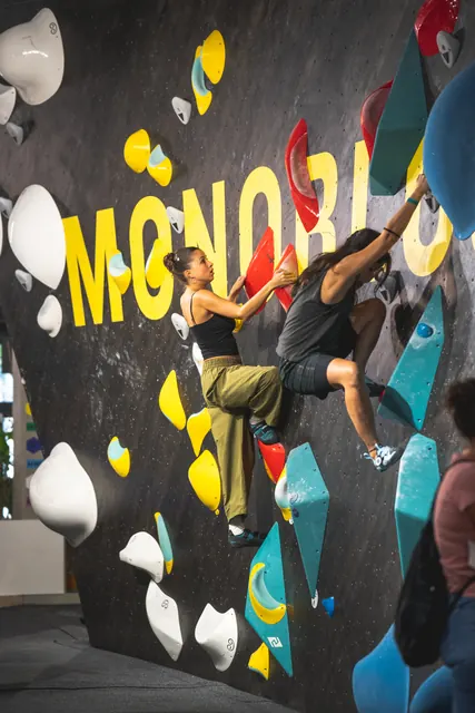 Two people climbing side by side on the MONOBLOC lettering wall.