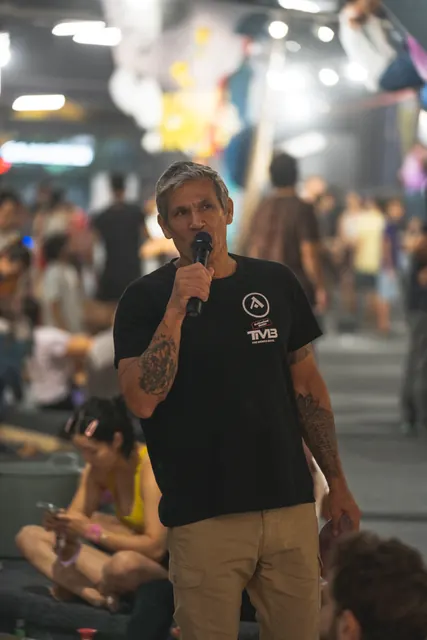 The host speaks into the microphone with the audience seated behind.