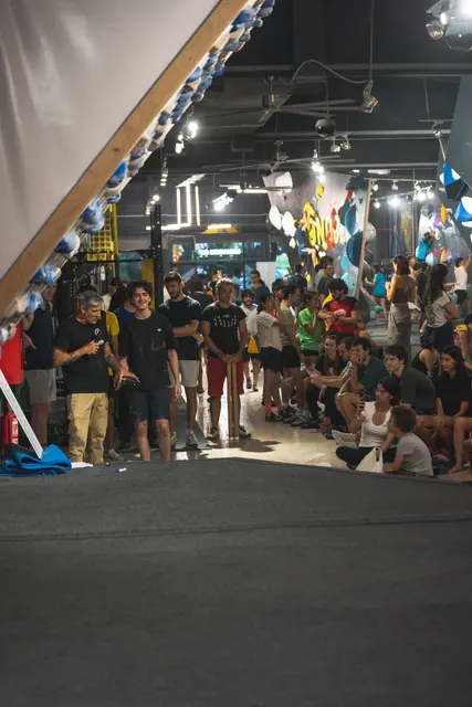 A crowd filling the gym and sitting on the mats during an event.